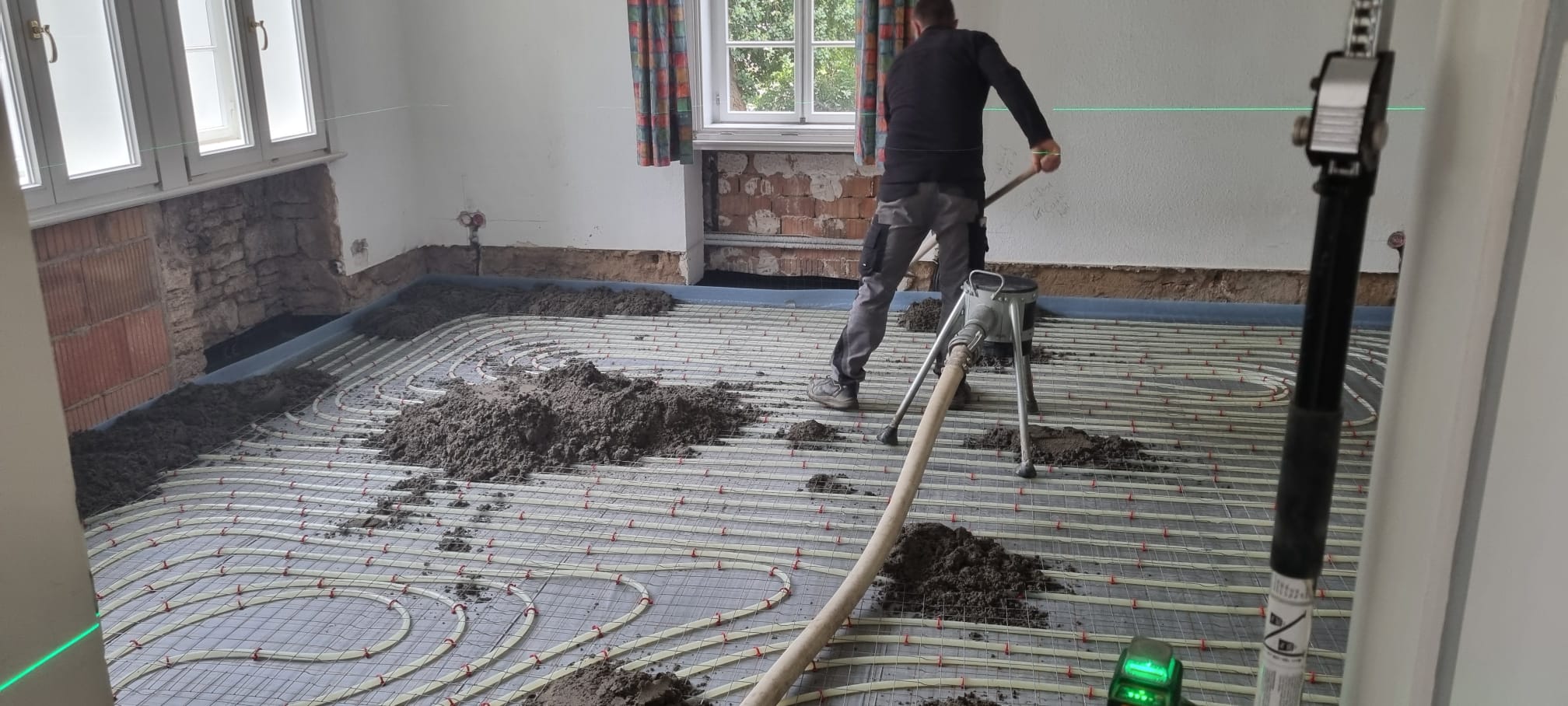 Handwerker beim Einbringen des Estrichs über den Fußbodenheizungsrohren mit Laser-Höhenkontrolle